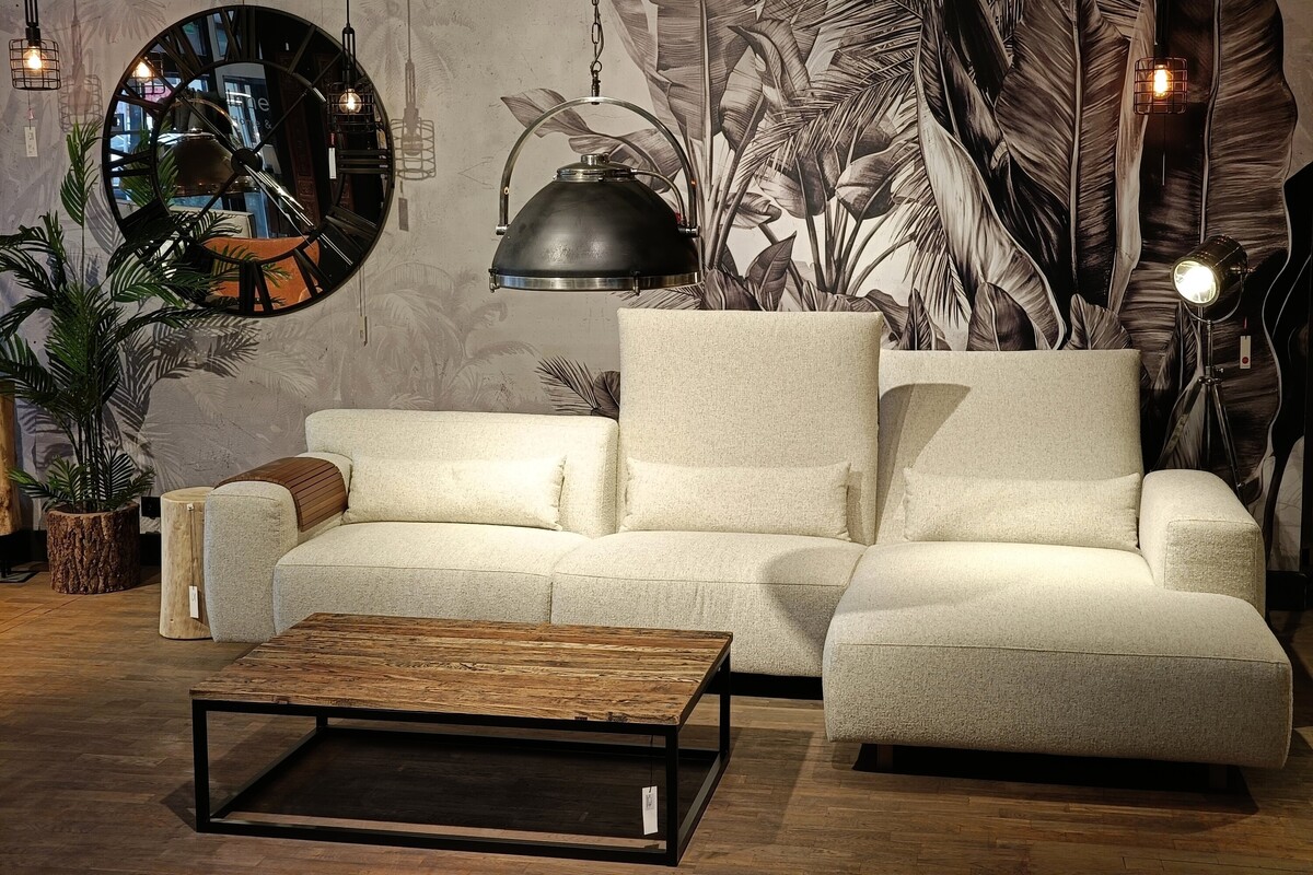 Duży narożnik modułowy, jasna kanapa na tle betonowej ściany, sofa Vesta Mti Furninova z ruchomymi zagółwkami, kanapy narożne Inne Meble Katowice, duży zegar na ścianie, stolik z drewna z recyklingu