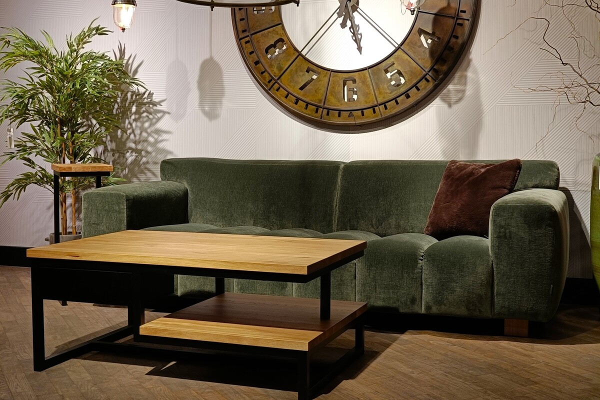 Welurowa sofa, pikowana kanapa, brązowy zegar na beżowej ścianie, stolik kawowy z półką