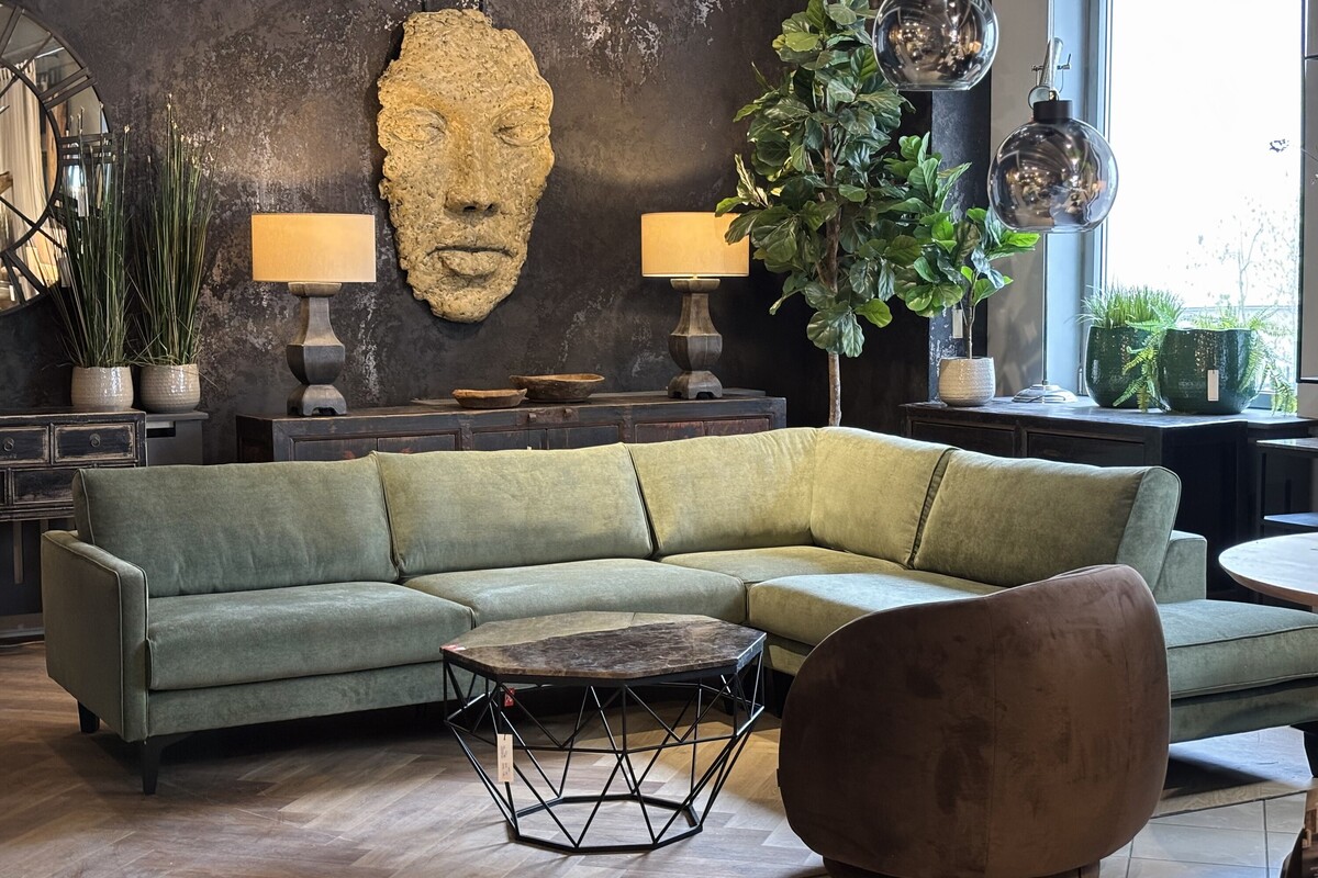Płaskorzeźba twarz na tle czarnej ściany. Duży zielony narożnik do salonu. Ciekawy stolik z kamiennym blatem. Brązowy fotel obrotowy.