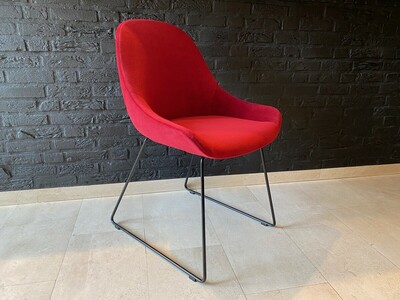 czerwone krzesło kubełkowe na metalowych płozach. Delikatne czarne nóżki nadają lekkości i charakteru